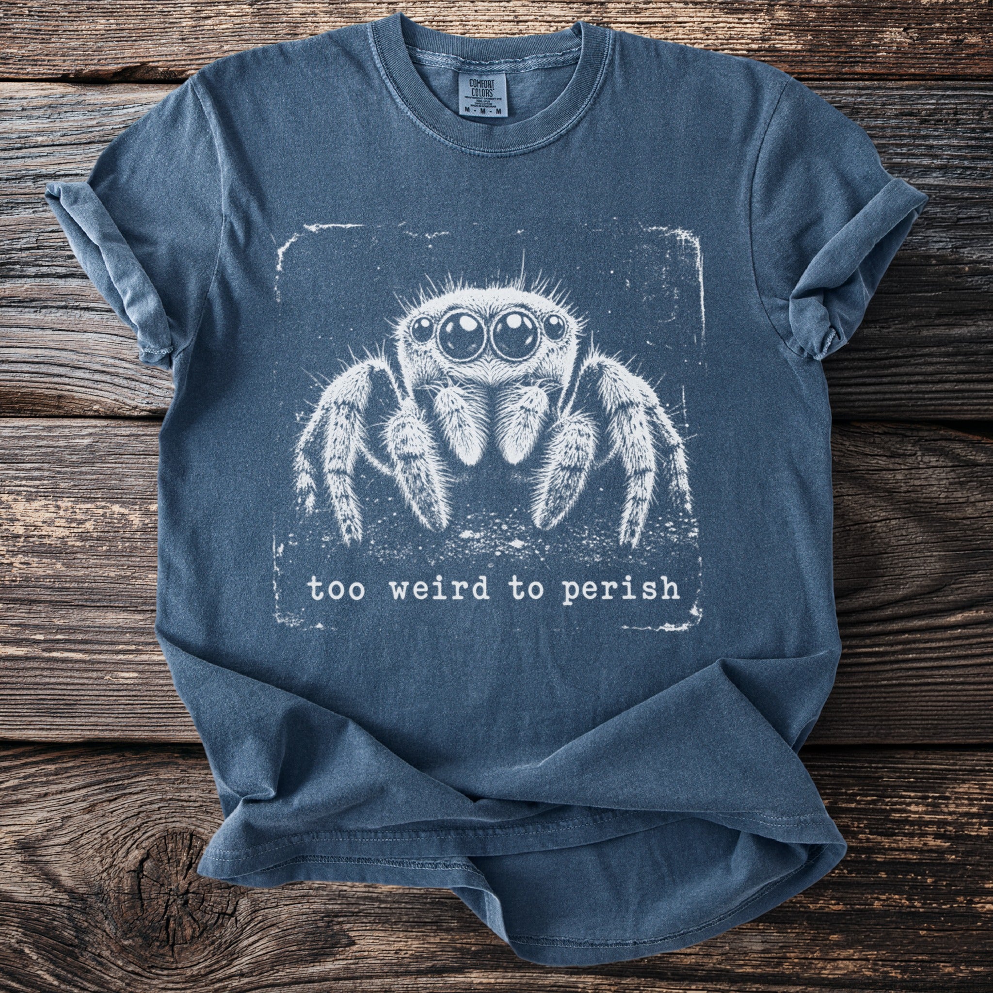 Blue t-shirt with white jumping spider graphic and text "too weird to perish".