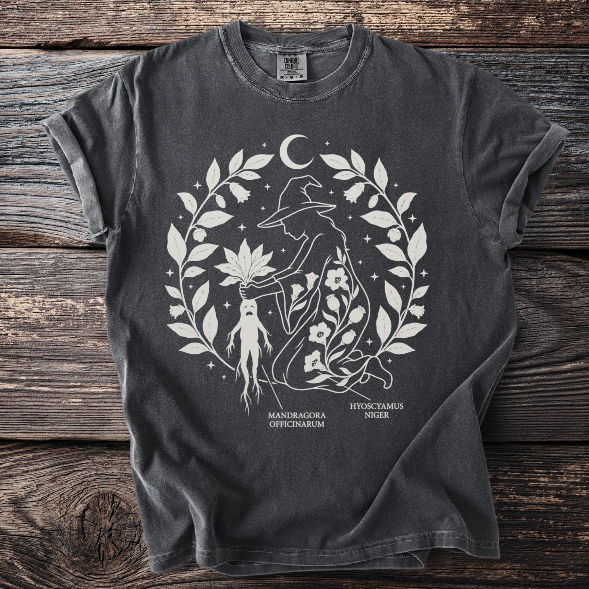 Dark gray t-shirt with white line art of a witch harvesting a mandrake plant.