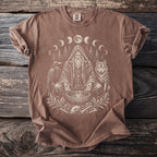 T-shirt featuring a central shamanic figure, wolf, raven, moon phases, and woodland elements.