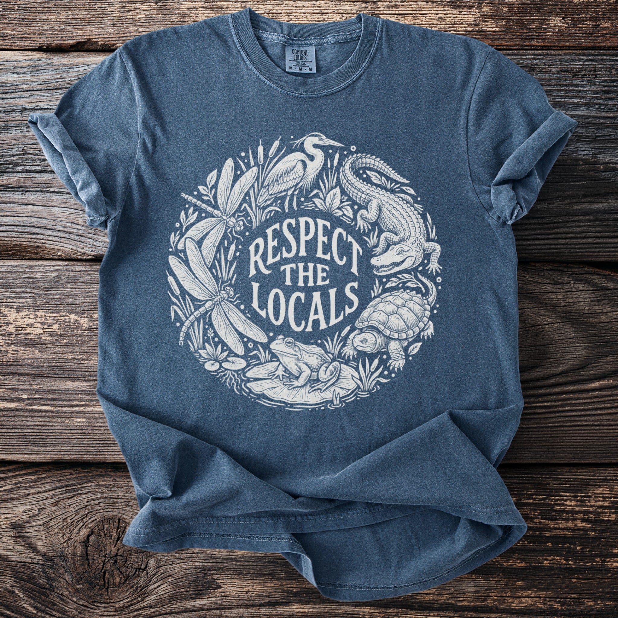 Blue t-shirt with white graphic of nature: alligator, turtle, frog, dragonflies, and heron.