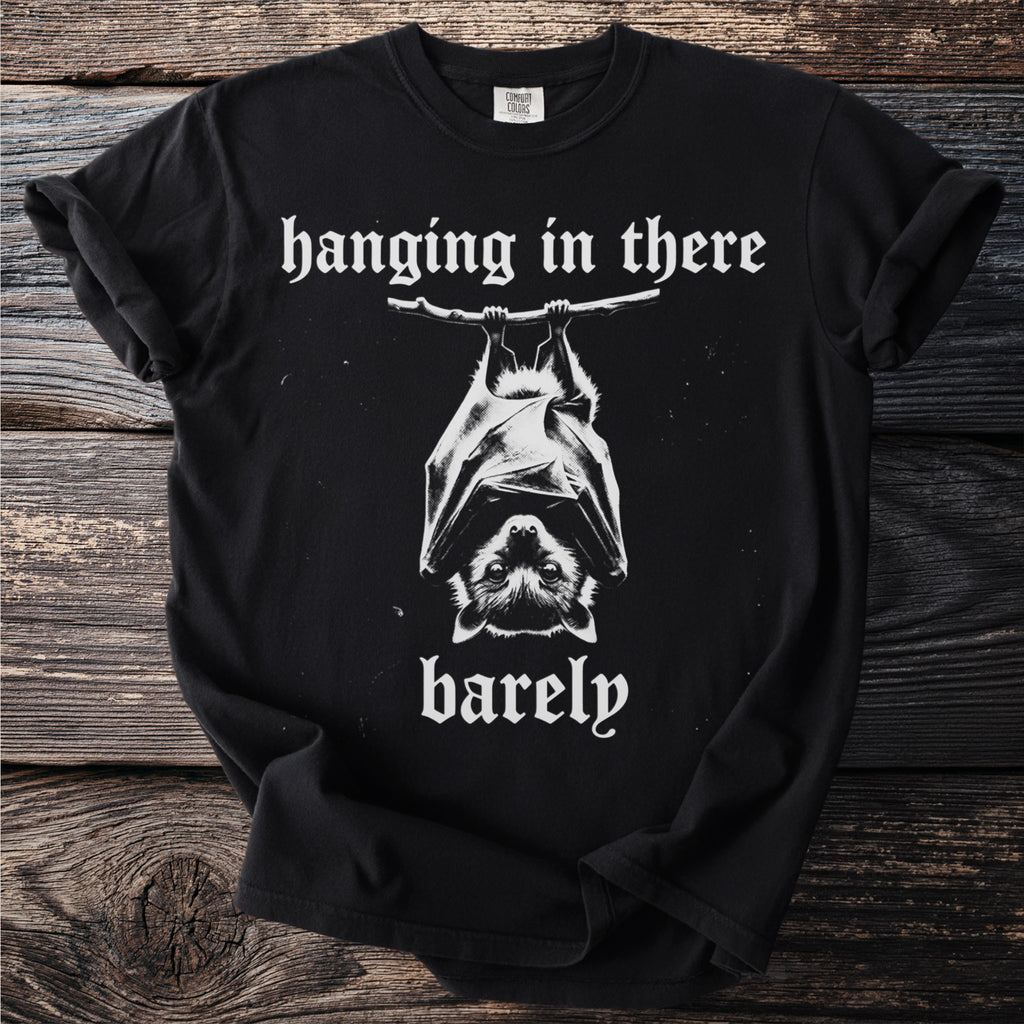 Black t-shirt with white text reading "hanging in there barely" and a bat graphic.