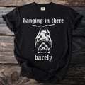 Black t-shirt with white text reading "hanging in there barely" and a bat graphic.