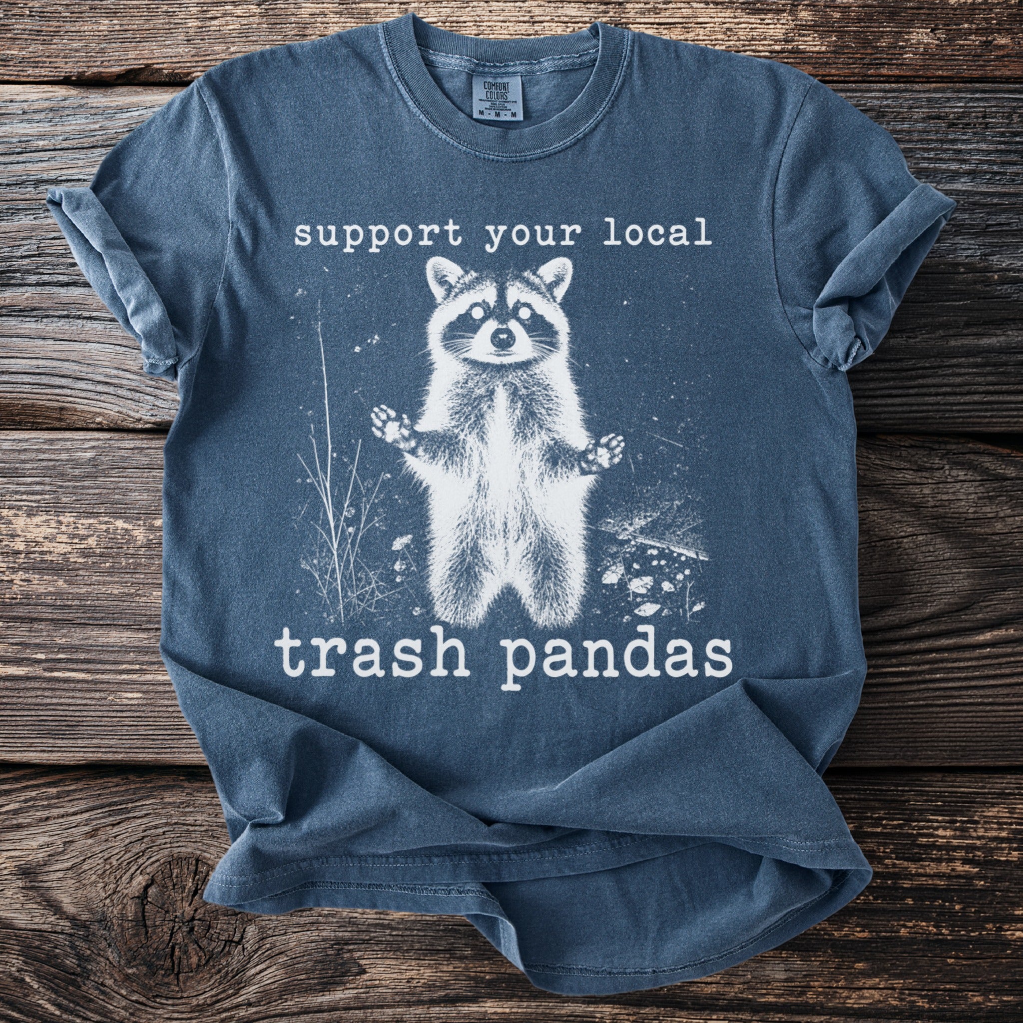 Blue t-shirt with graphic of a raccoon and text "support your local trash pandas".