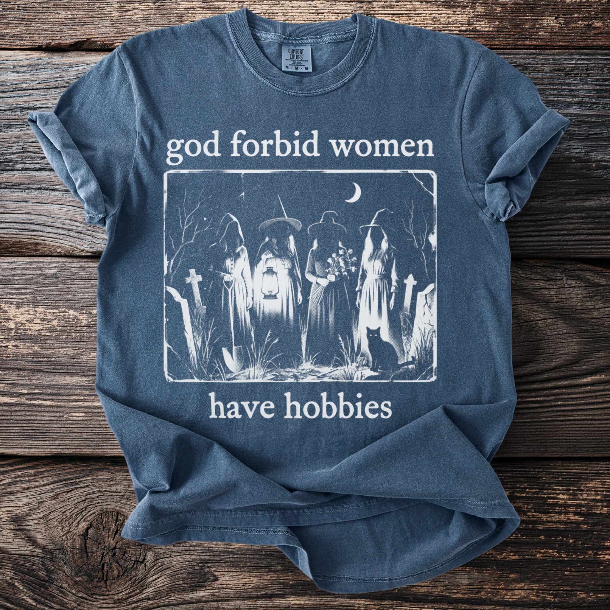 T-shirt with "god forbid women have hobbies" text and witch illustration.