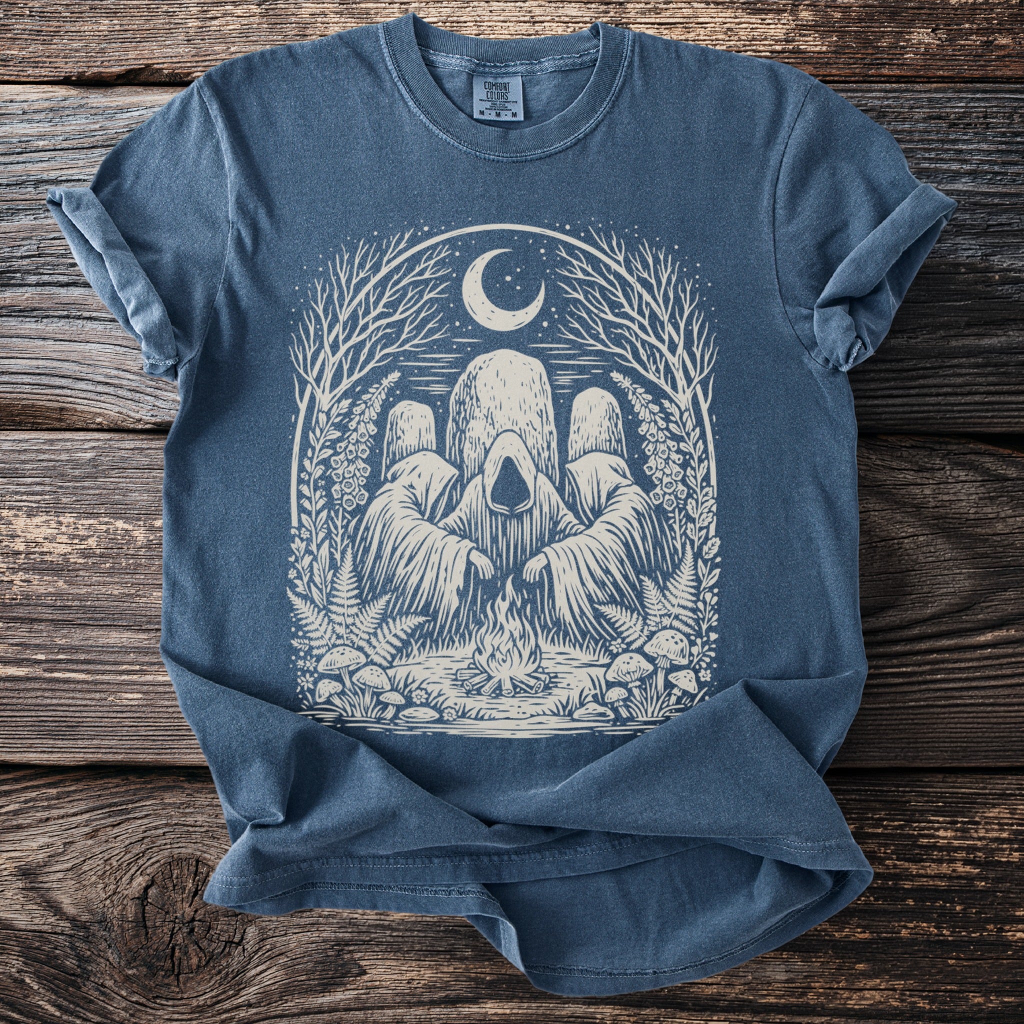 Blue t-shirt with a graphic of three hooded figures around a campfire under a moon.