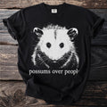 Black t-shirt with white possum graphic and "possums over people" text.