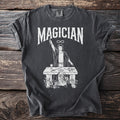 Dark gray t-shirt with "Magician" text and a mystical figure over a table.