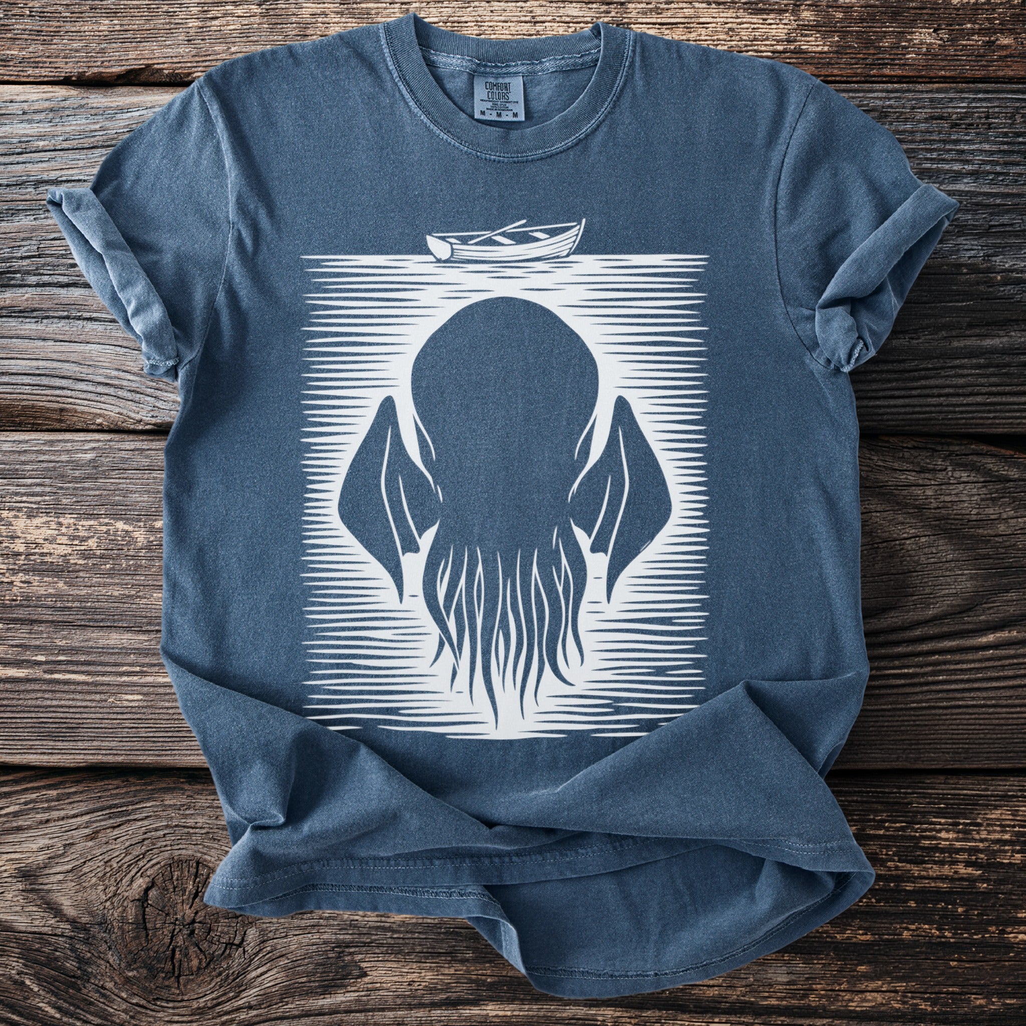 Blue t-shirt with white graphic of a large squid-like creature and a small boat.