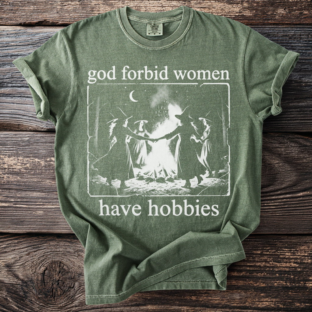 Green t-shirt with "god forbid women have hobbies" text and witch graphic.