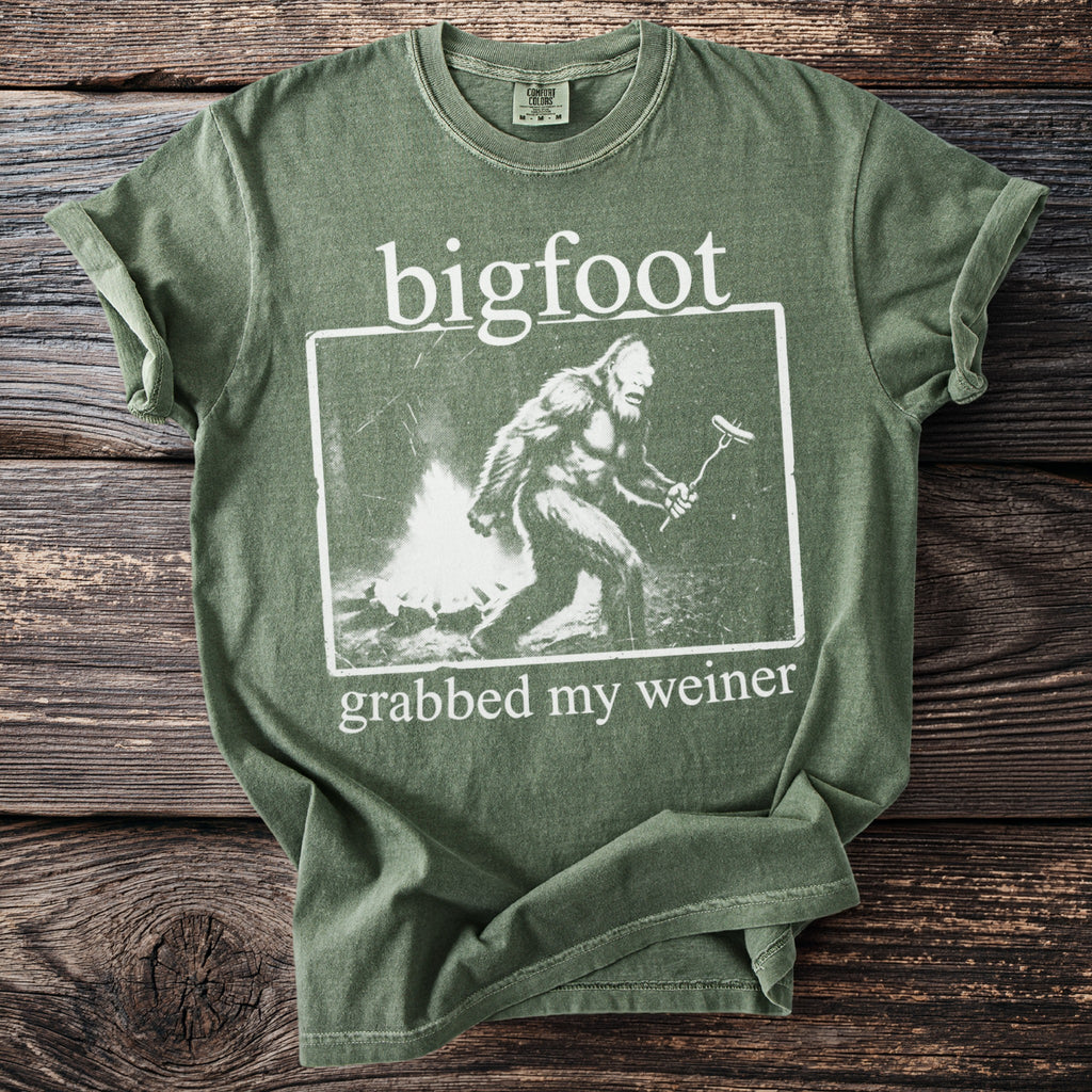 Green t-shirt featuring a graphic of a Bigfoot with the text "bigfoot grabbed my weiner".
