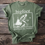 Green t-shirt featuring a graphic of a Bigfoot with the text "bigfoot grabbed my weiner".