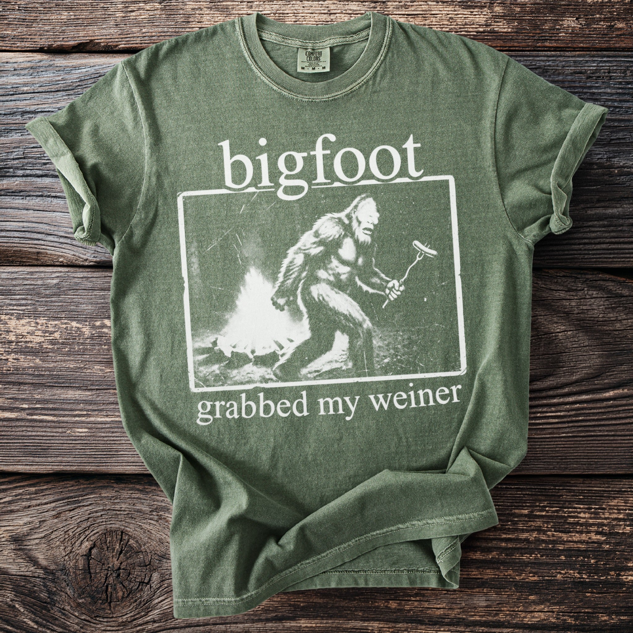 Green t-shirt featuring a graphic of a Bigfoot with the text "bigfoot grabbed my weiner".