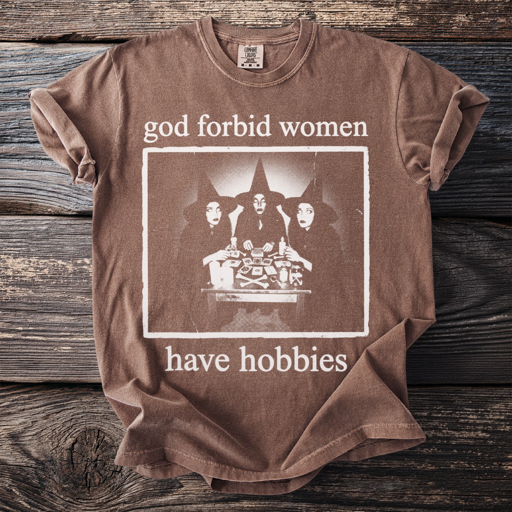 Brown t-shirt with "god forbid women have hobbies" text and witch graphic.