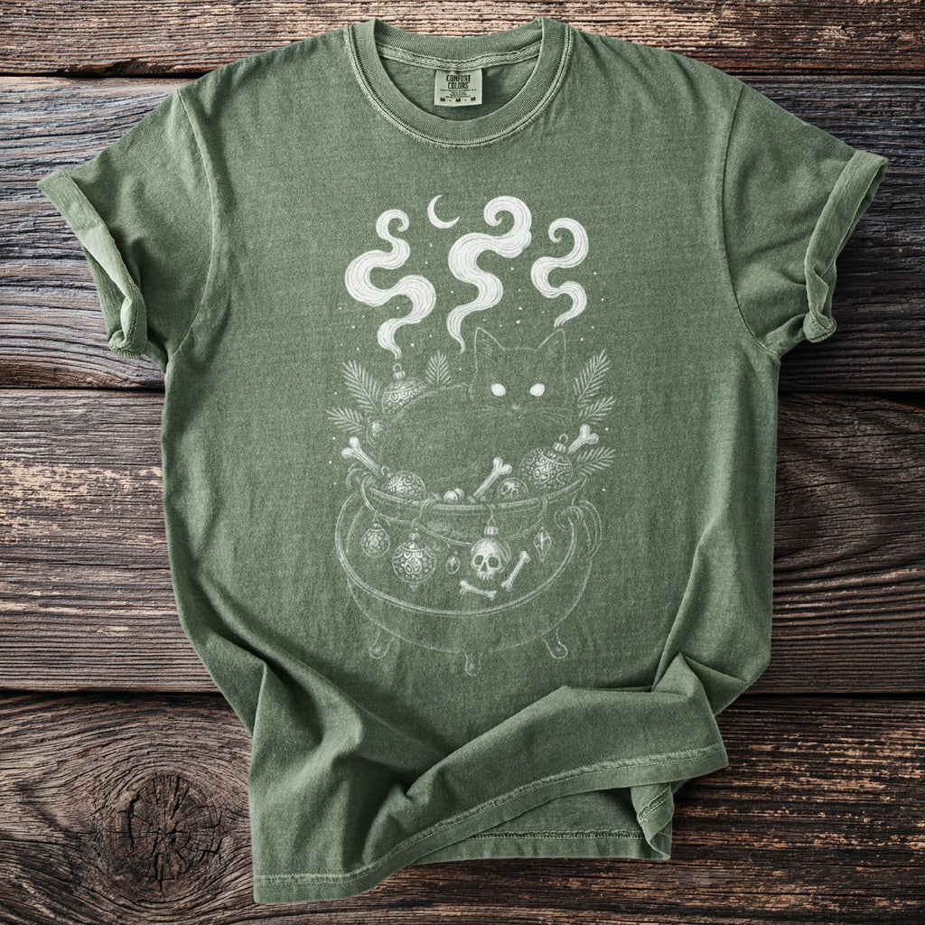 Green t-shirt with a black cat in a cauldron filled with bones and ornaments.