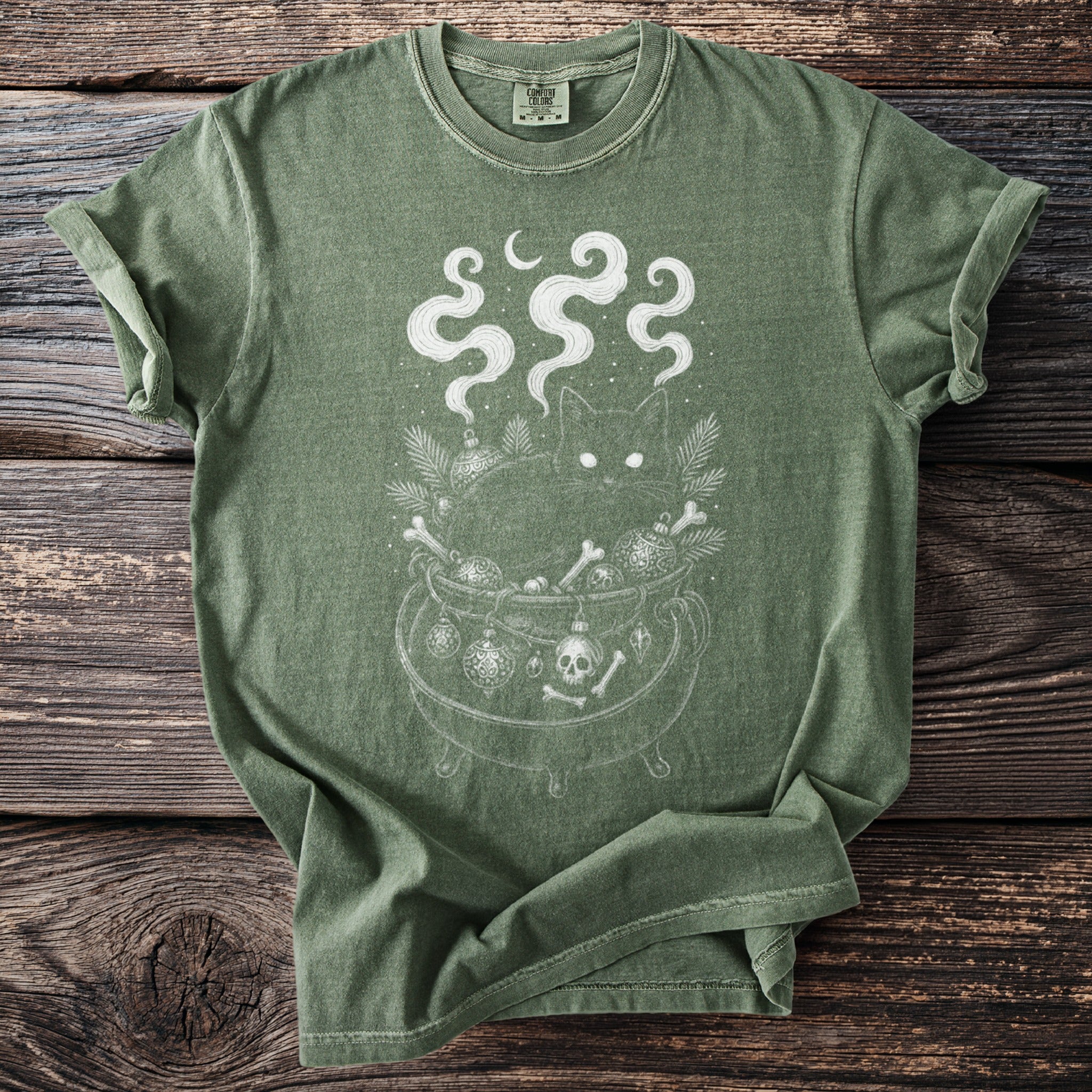 Green t-shirt with a black cat in a cauldron filled with bones and ornaments.