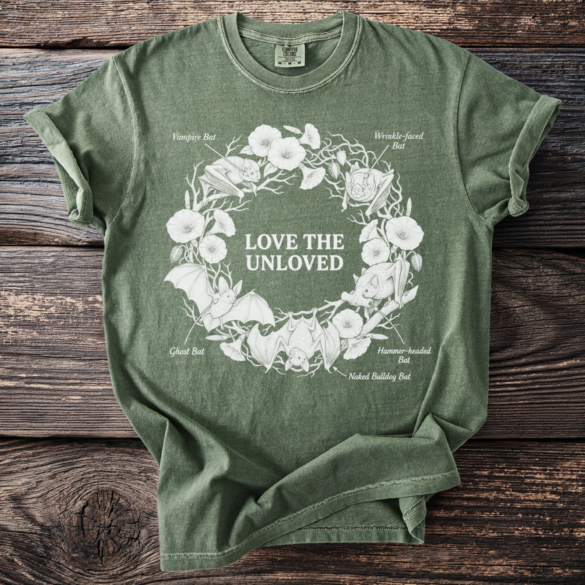 Green t-shirt with white graphic of bats and flowers, text "LOVE THE UNLOVED".