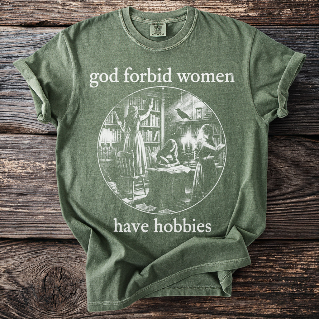 Green t-shirt with "god forbid women have hobbies" text and illustration of women in a library.