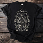 Black t-shirt with charcoal sketch of a person with snake, wolf mask, crescent moon, and flames.