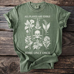 Green t-shirt with skull and crossbones and botanical illustrations. "ALL PLANTS ARE EDIBLE SOME ONLY ONCE."