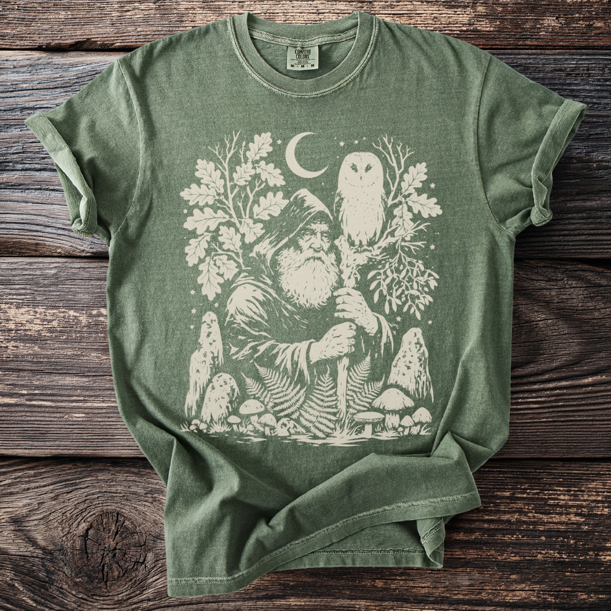 Green t-shirt with a white graphic of a hooded wizard, owl, moon, trees, and mushrooms.