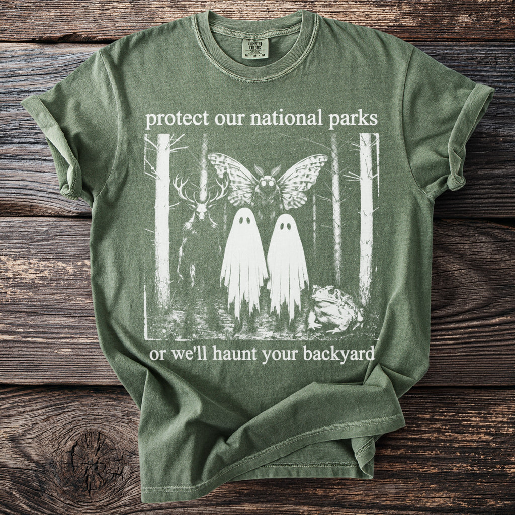 Green t-shirt with "protect our national parks or we'll haunt your backyard" text and a forest graphic.