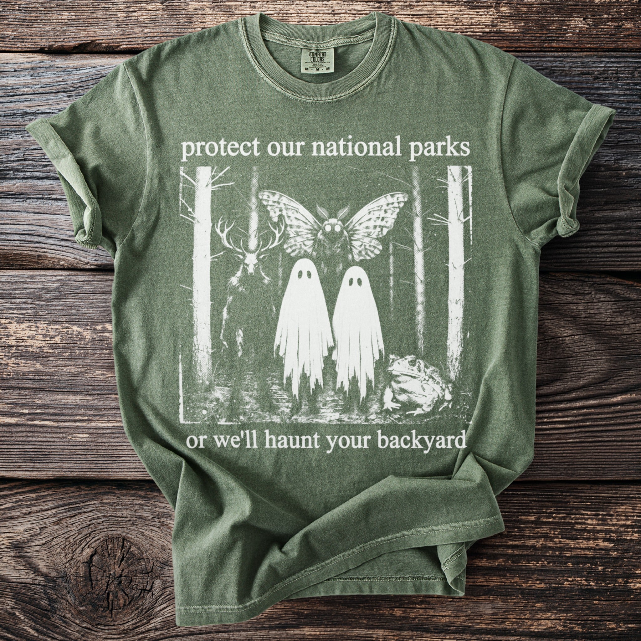 Green t-shirt with "protect our national parks or we'll haunt your backyard" text and a forest graphic.