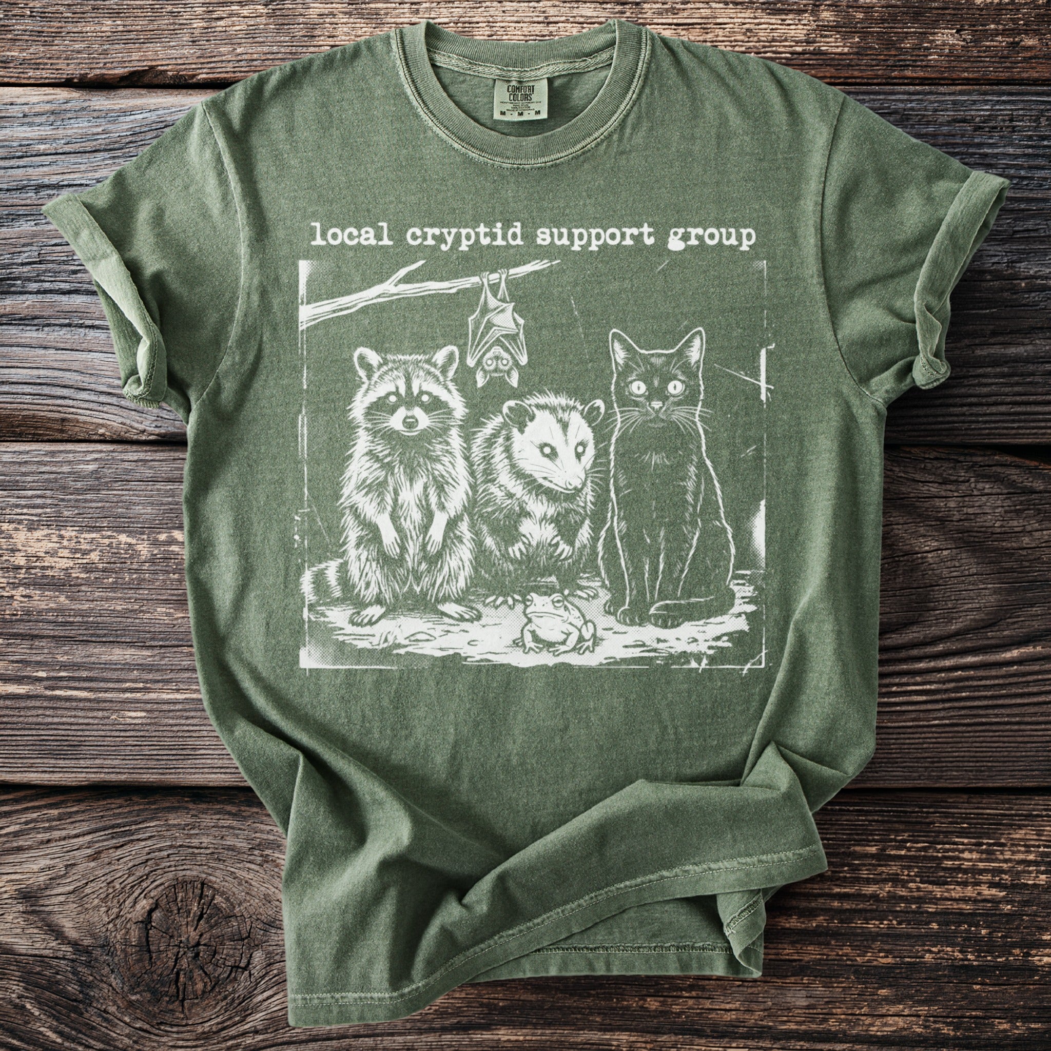 Green t-shirt with 'Local Cryptid Support Group' text and illustration of a raccoon, opossum, cat, bat, and frog.