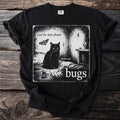 Black t-shirt with graphic featuring a black cat, moth, spider, and text "you're not alone there are bugs".