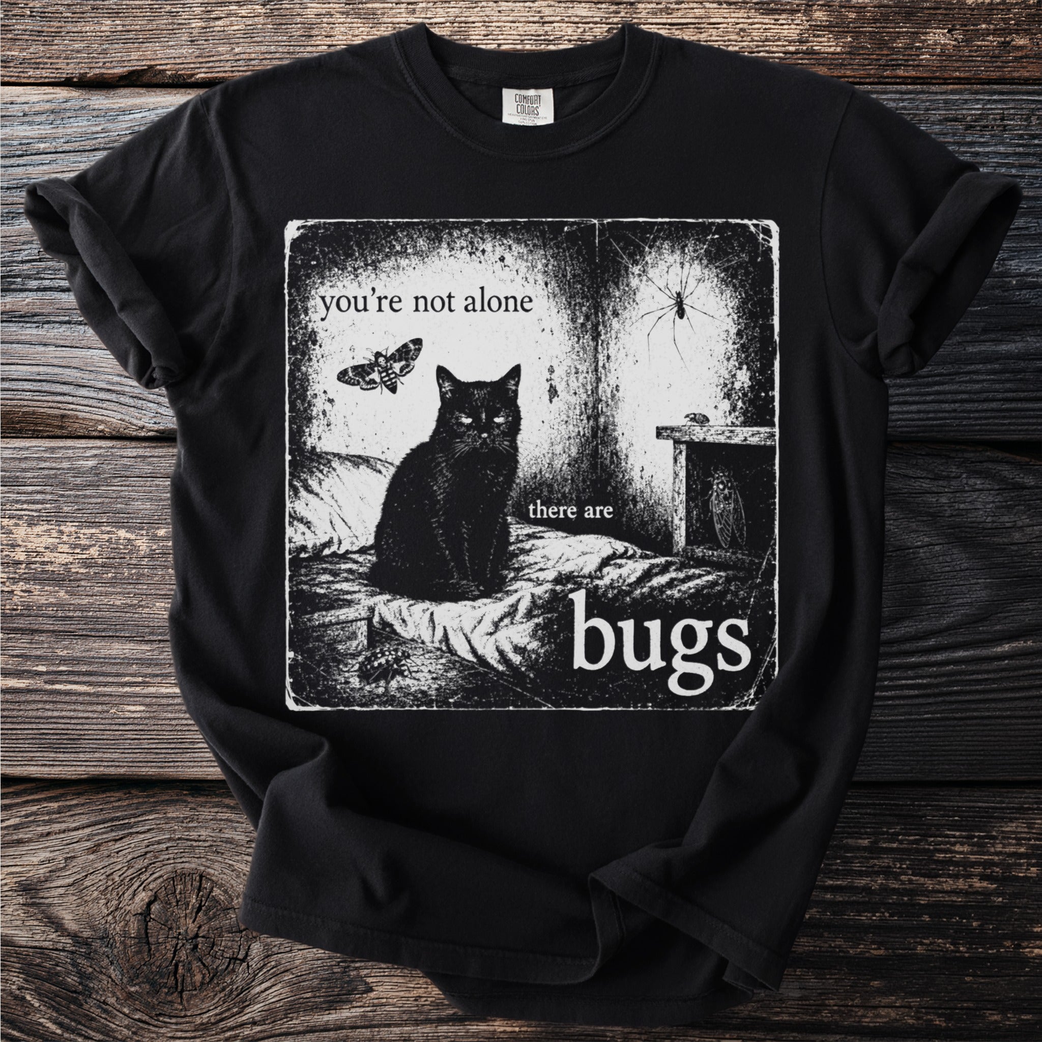 Black t-shirt with graphic featuring a black cat, moth, spider, and text "you're not alone there are bugs".