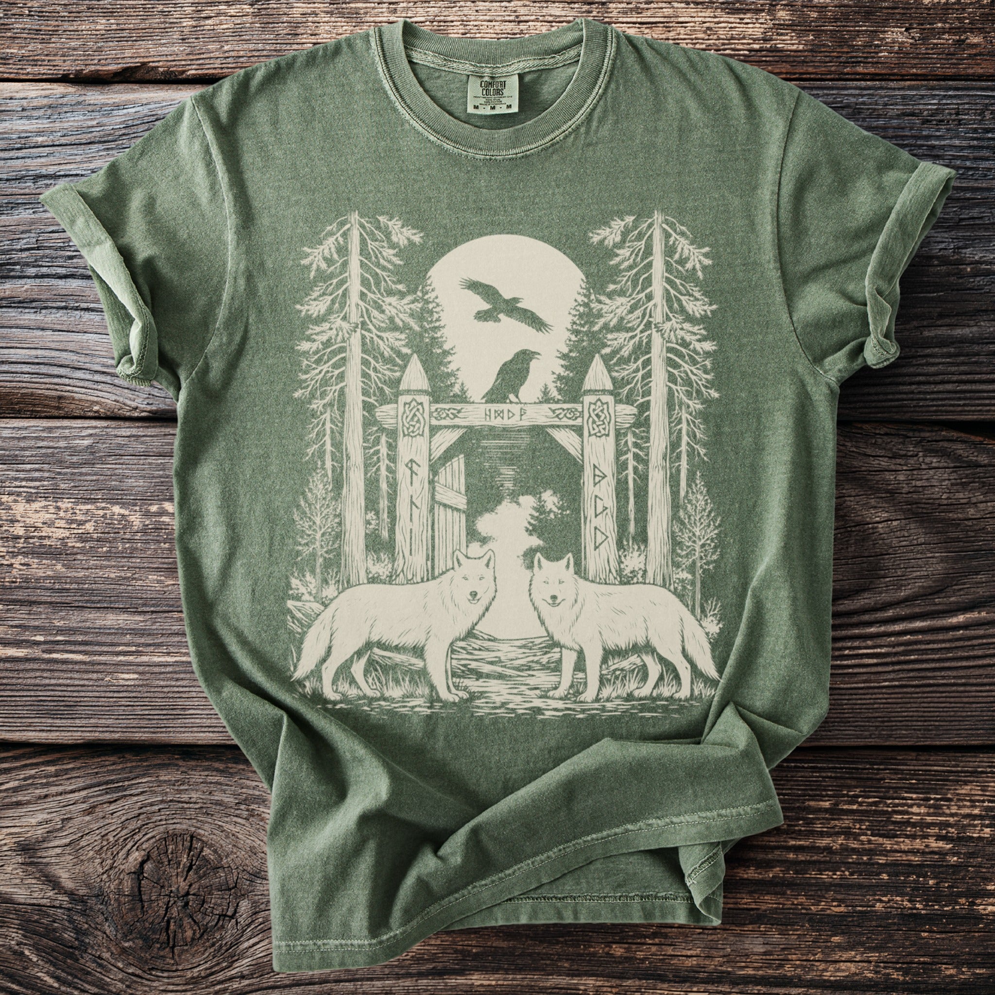 Green t-shirt with graphic of two wolves, trees, a gate, and ravens.