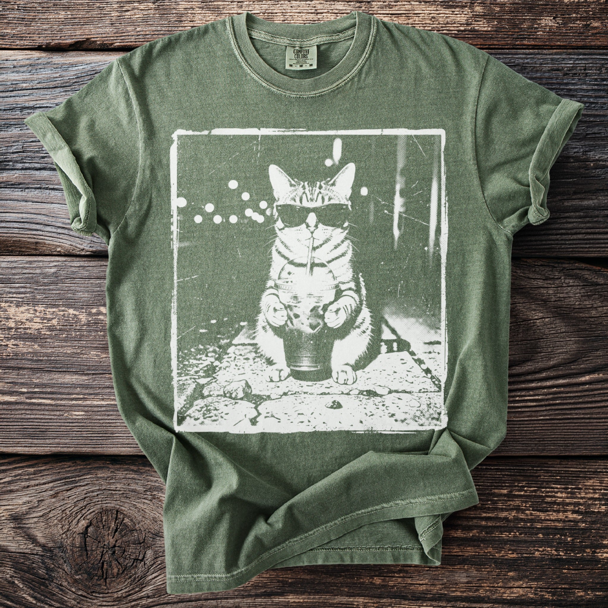 Green t-shirt with a white graphic of a cat wearing sunglasses, drinking from a cup.