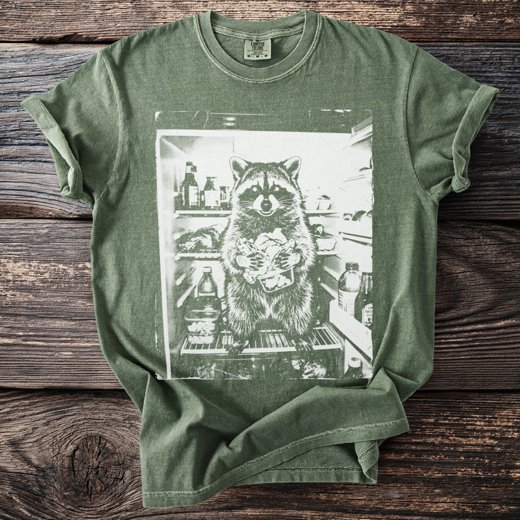 Green t-shirt with graphic of a raccoon holding food in a refrigerator.