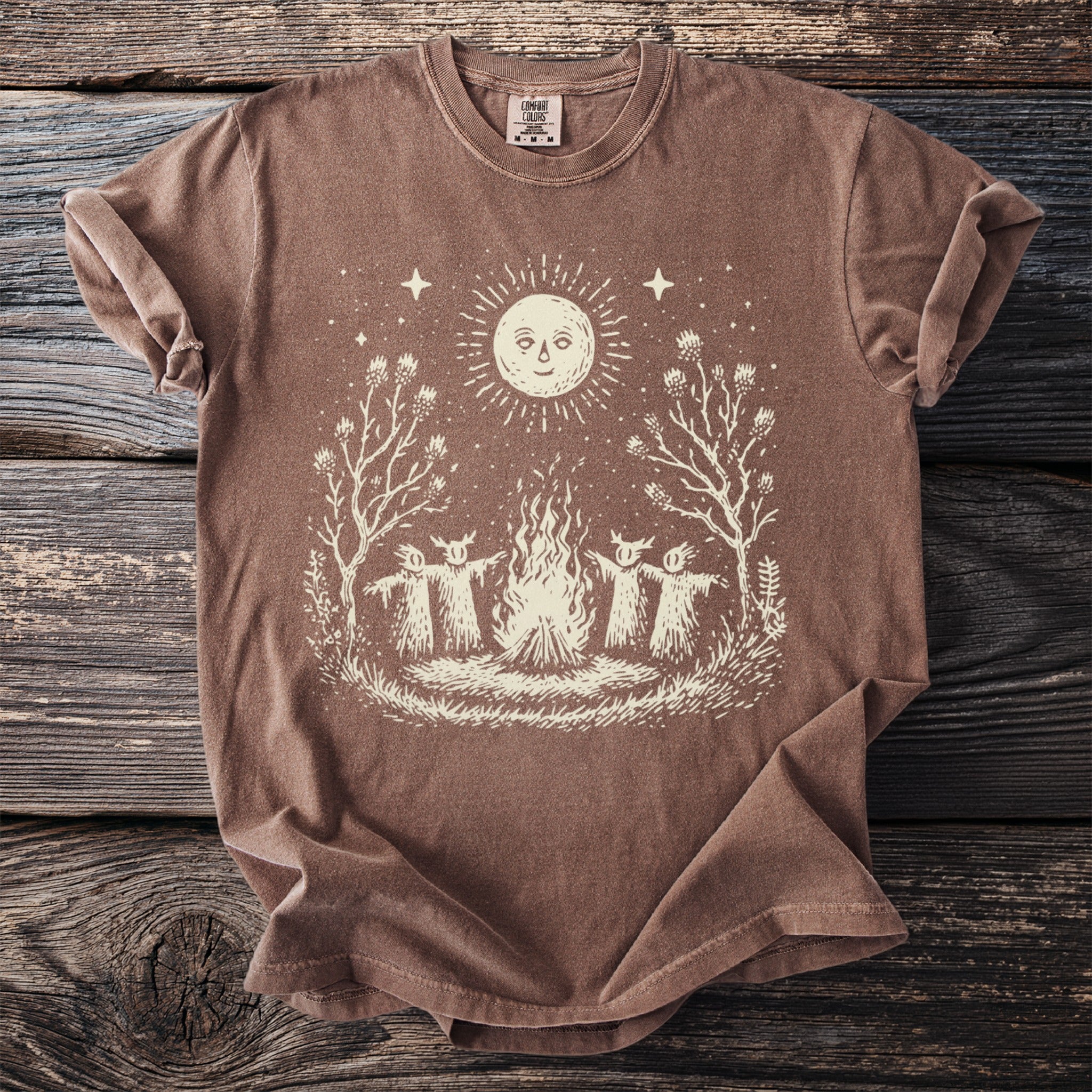 Brown t-shirt with a sun, campfire, and figures surrounding the fire.