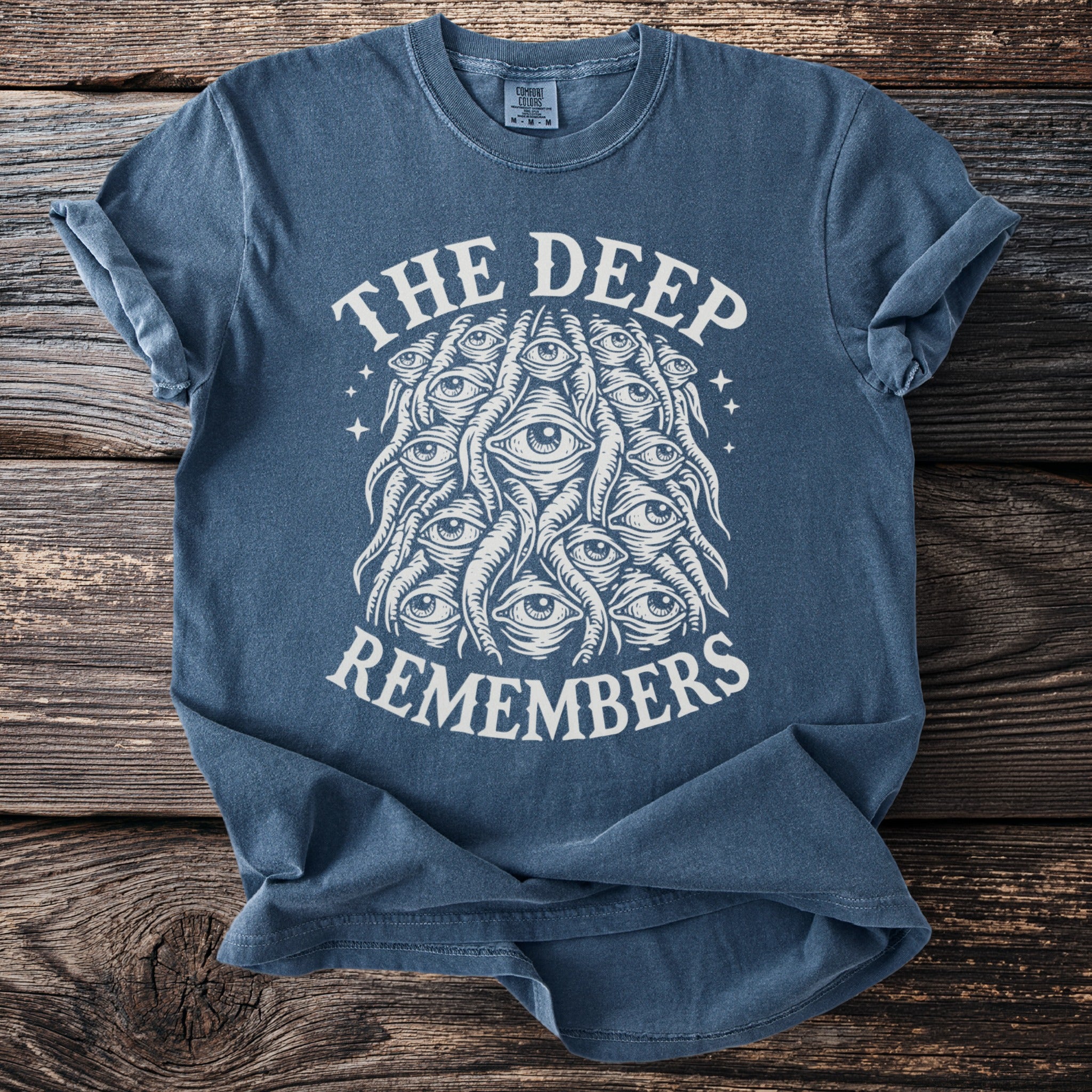 Blue t-shirt with white text "THE DEEP REMEMBERS" and an eye graphic.