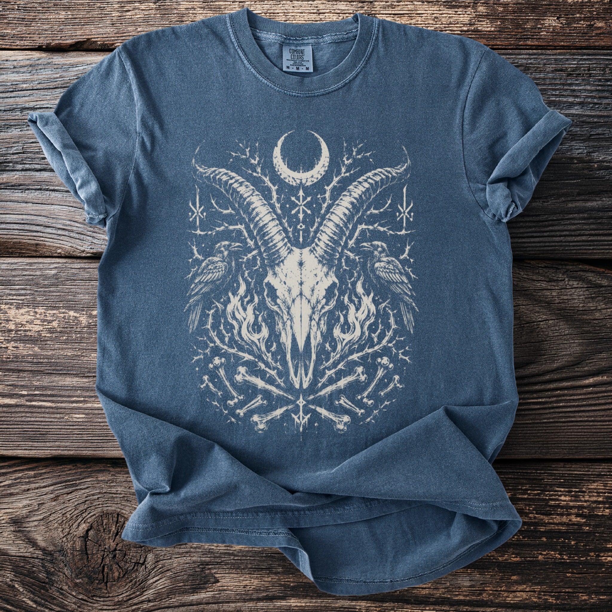 Blue t-shirt with a white graphic of a goat skull, ravens, and bones.