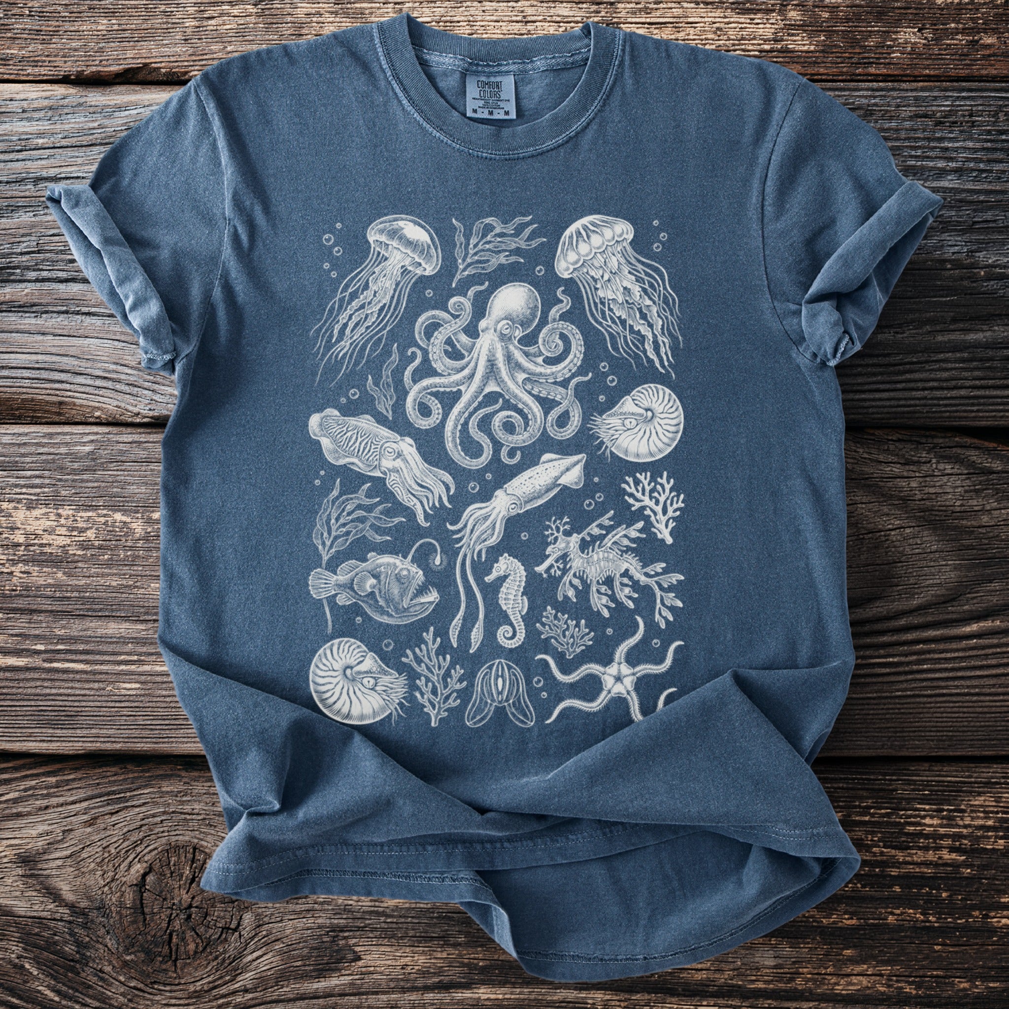 Blue t-shirt featuring a detailed white line drawing of various sea creatures and plants.