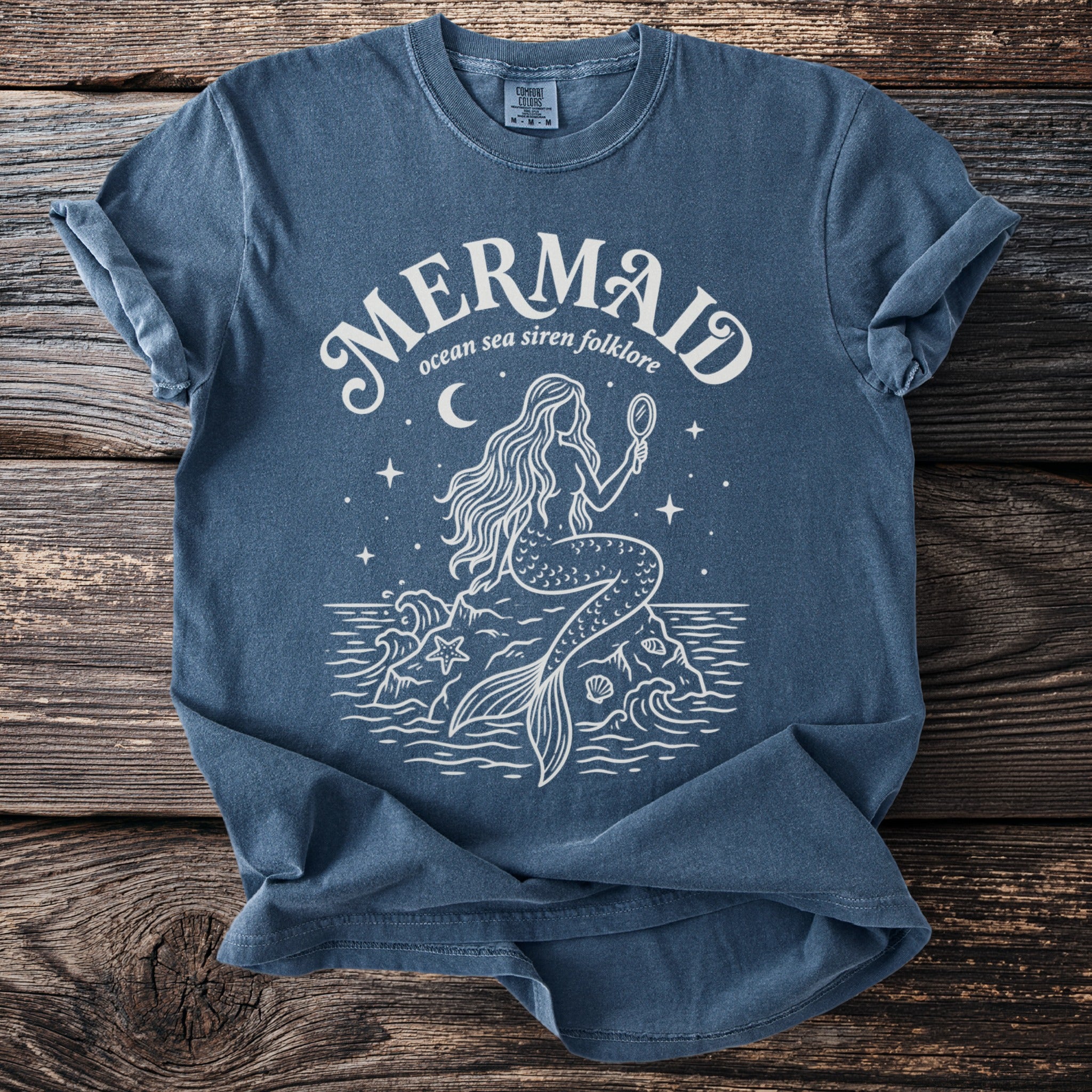 Blue t-shirt with a white line drawing of a mermaid holding a mirror.