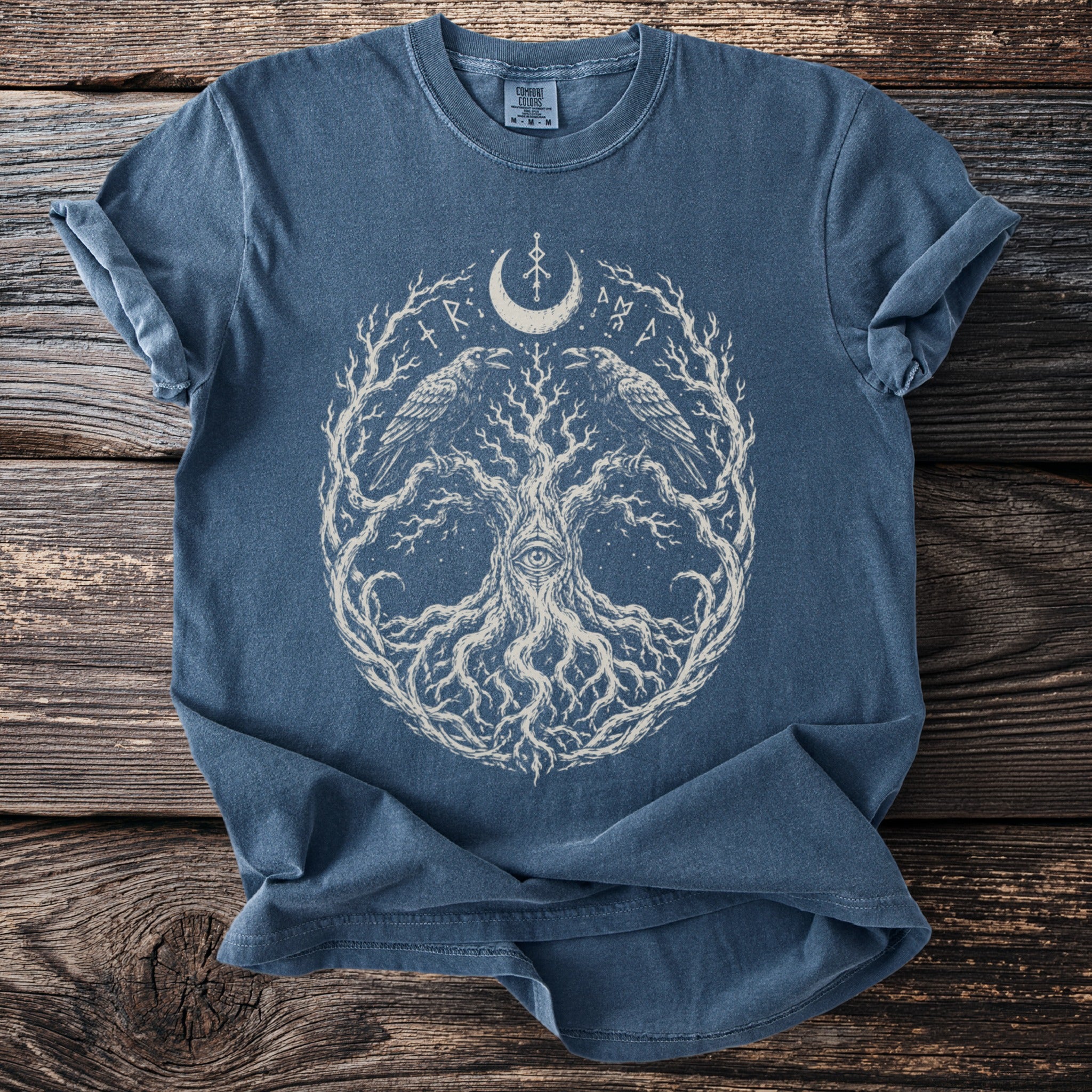 Blue t-shirt with a white graphic of a tree, ravens, eye, and moon symbols.