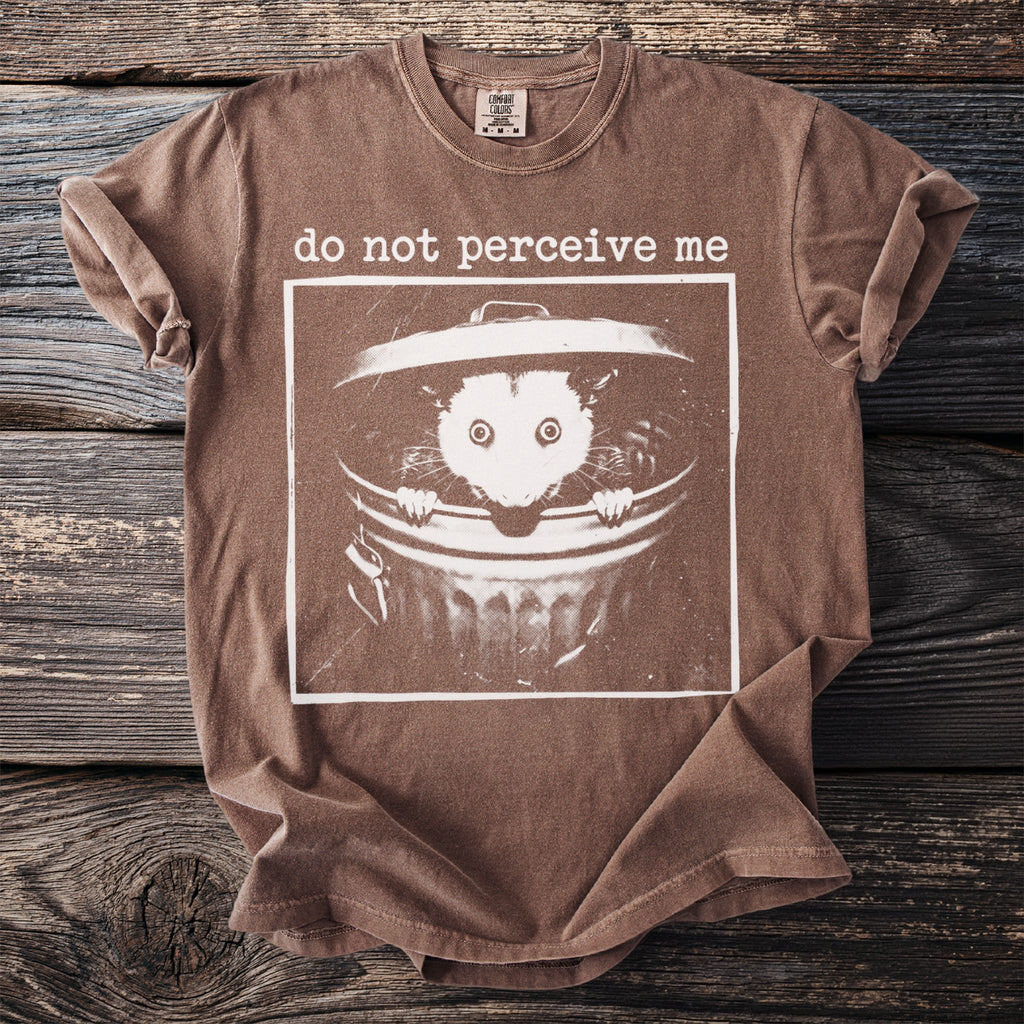Brown t-shirt with graphic of an opossum in a trash can and text "do not perceive me".