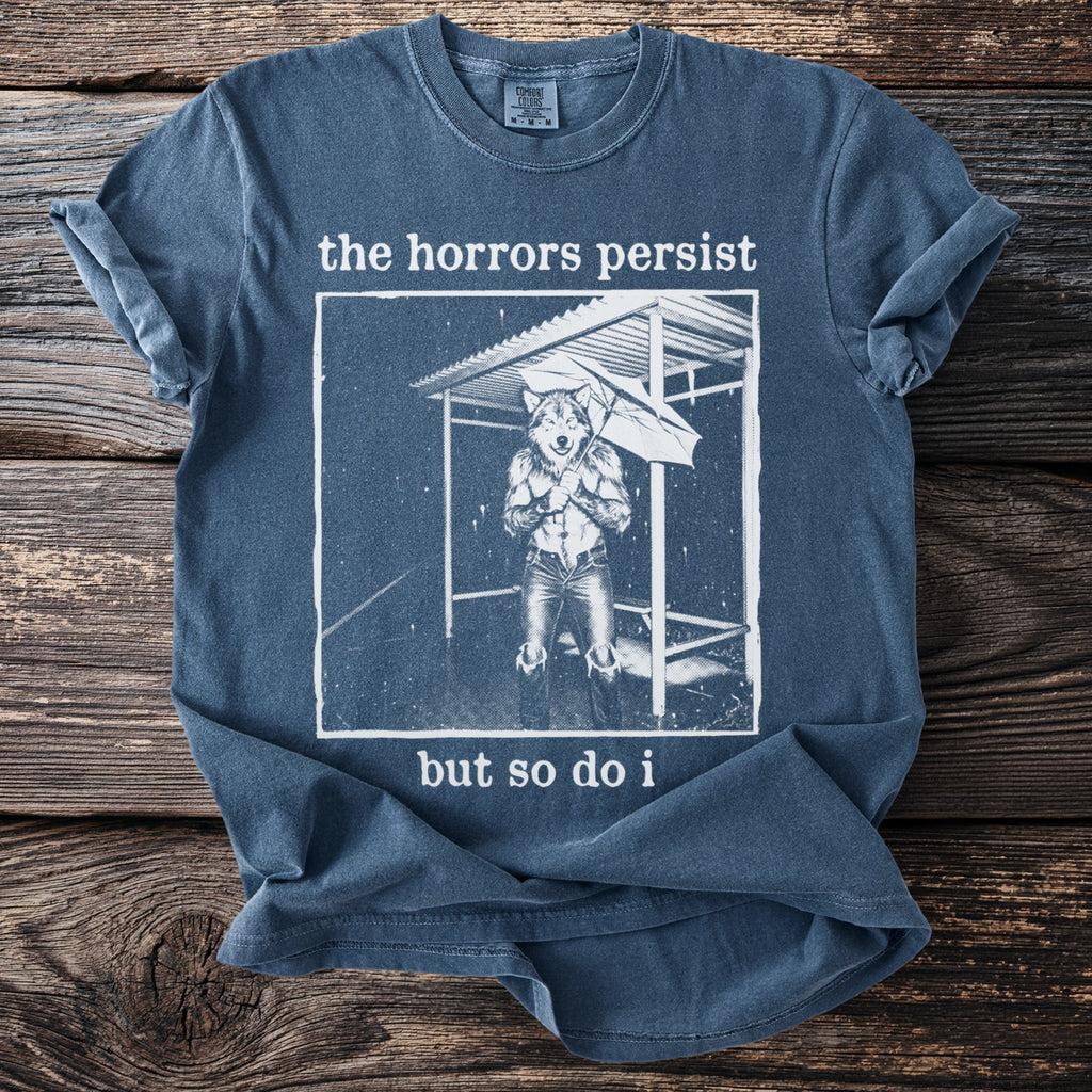 Blue t-shirt with graphic of anthropomorphic wolf holding umbrella, text "the horrors persist but so do i".