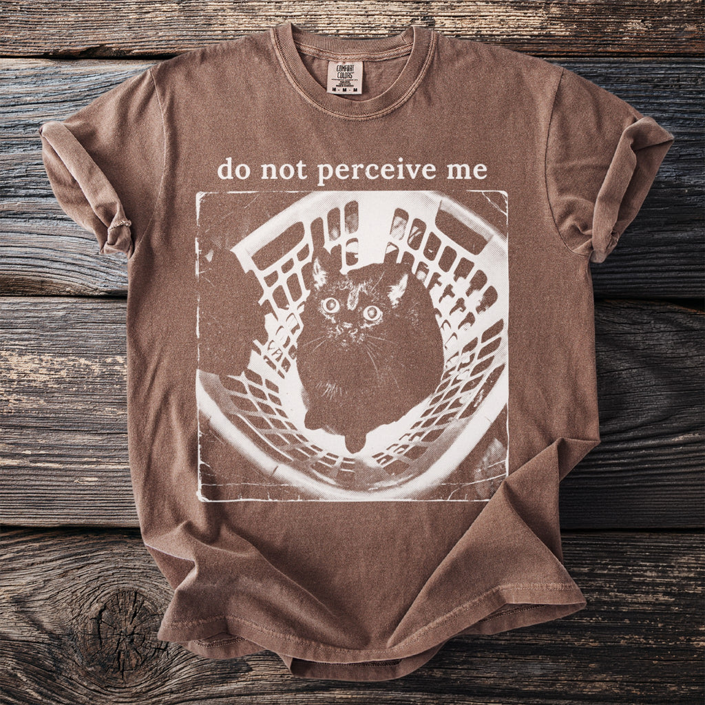 Brown t-shirt with a distressed graphic of a cat in a basket and text "do not perceive me".