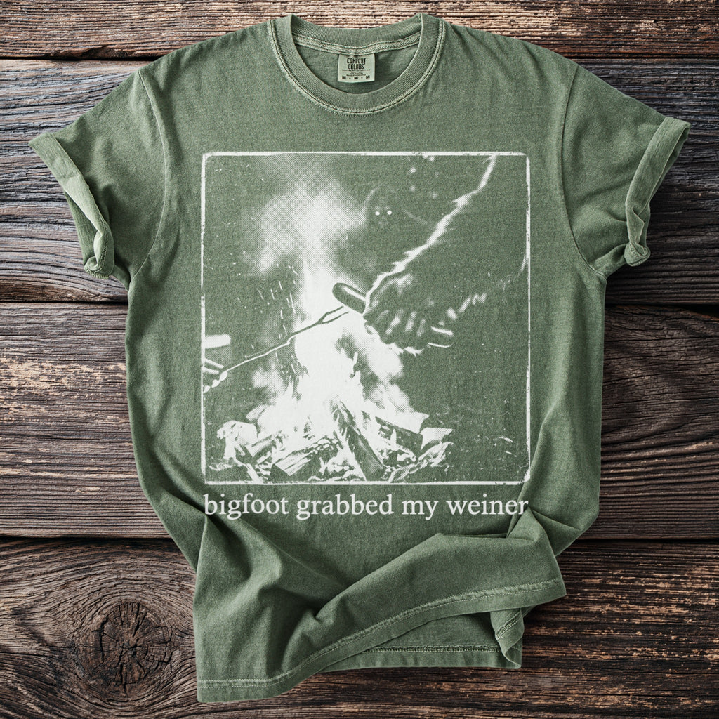 Green t-shirt with Bigfoot grabbing a hot dog over a campfire with text.