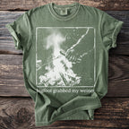 Green t-shirt with Bigfoot grabbing a hot dog over a campfire with text.
