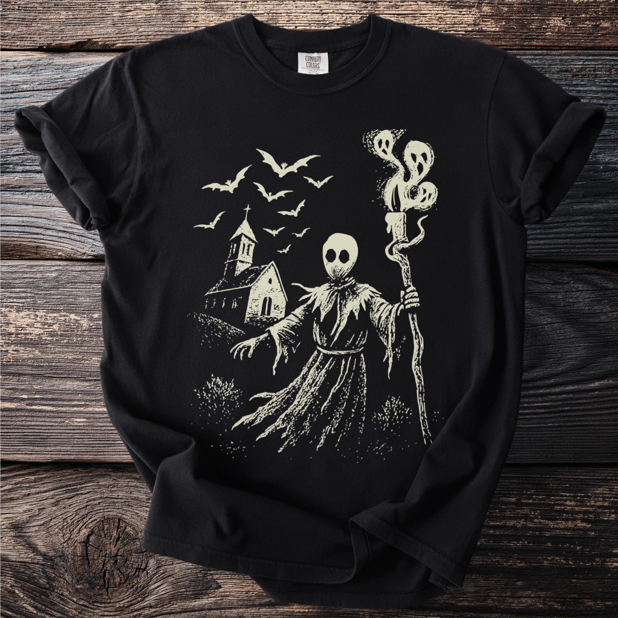 Black t-shirt with a cream gothic illustration of a figure holding a staff with three ghosts.