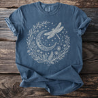 Blue t-shirt with a white line drawing of a crescent moon, dragonfly, stars, and plants.