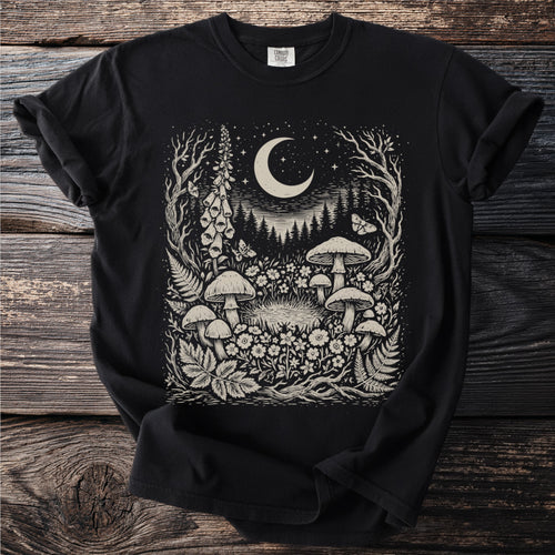 Black t-shirt with a cream-colored linocut of a forest scene featuring mushrooms, moon, and stars.