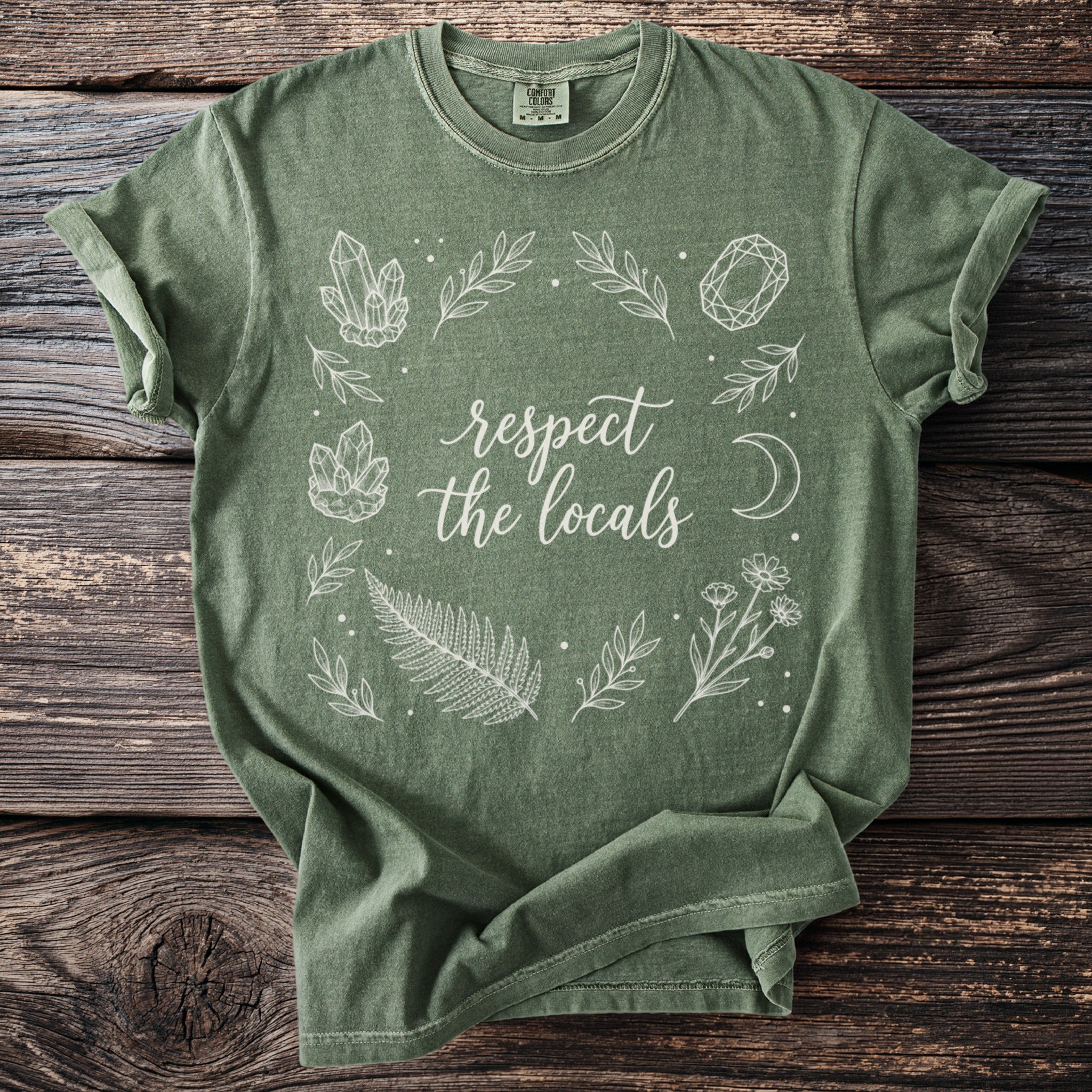 Green t-shirt with "respect the locals" text and crystals, leaves, moon and flowers design.