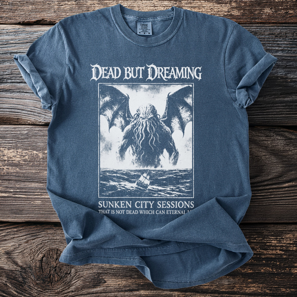 Blue t-shirt with "DEAD BUT DREAMING" and tentacled creature graphic.