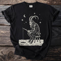 Black t-shirt with a cream folk-cut print: Krampus sits on a three-legged stool on the ice, a fishing line down a small hole.