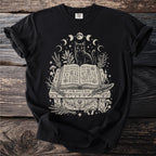 Black t-shirt featuring a black cat sitting on an open book with mystical symbols and celestial elements.